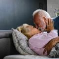 Eldre mann med skjegg omfavner eldre kvinne i sengen