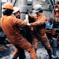Tre arbeidere i verneutstyr jobber med boring på oljeplattform