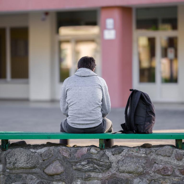 Gutt sittende med ryggen til på en benk i skolegården